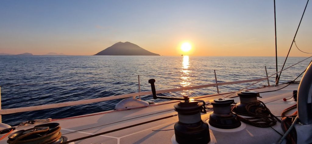 Nell'immagine è presente una barca per immergersi nella bellezza dei paesaggi marini al tramonto in primavera e all'orizzonte si vede un'isola
